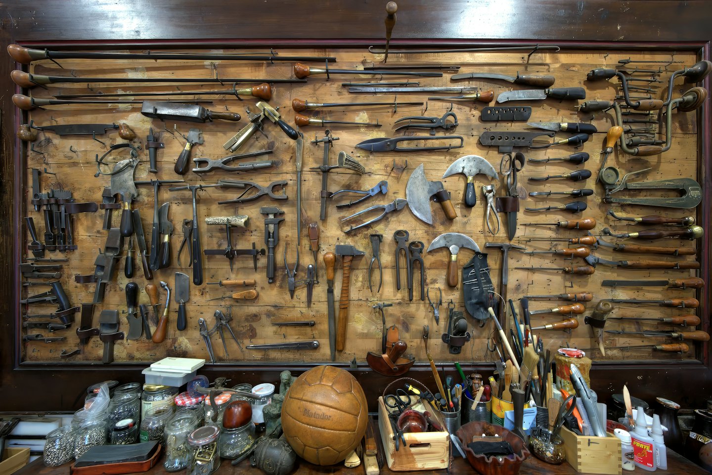 Antique tools displayed on a pegboard above a cluttered workbench.